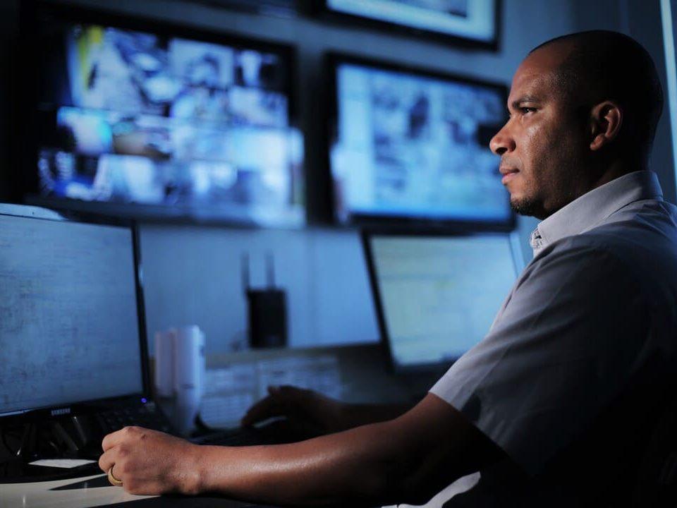 Profissional operando computadores em uma central de monitoramento e vigilância.