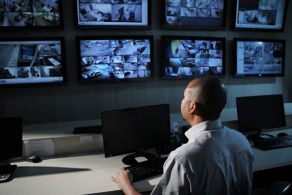 Profissional observando várias telas em uma central de monitoramento e vigilância.