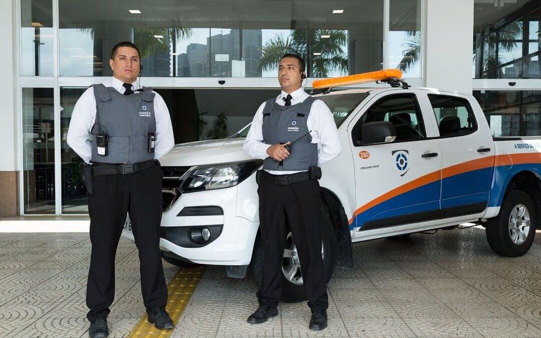 Dois vigilantes uniformizados em frente a uma caminhonete de segurança, transmitindo confiança e proteção.