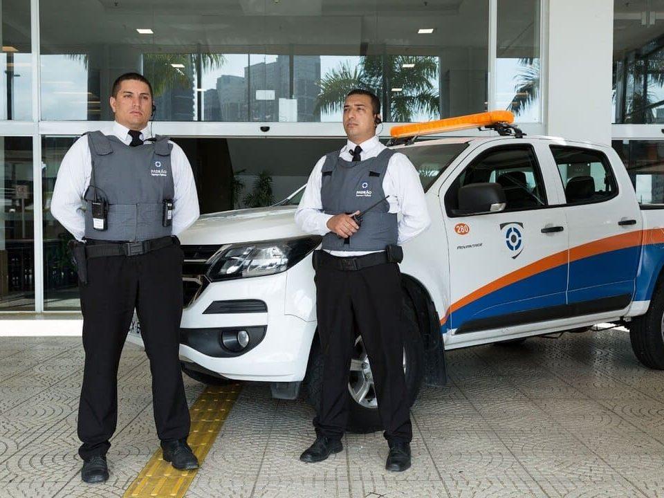 Dois vigilantes uniformizados em frente a uma caminhonete de segurança, transmitindo confiança e proteção.