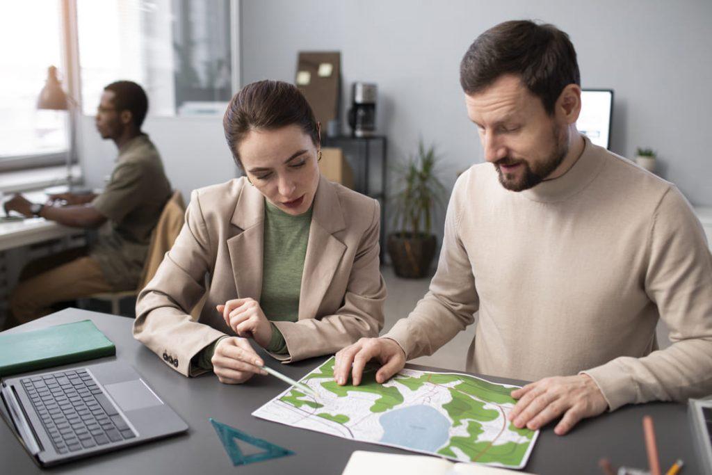 ✅ Texto alternativo (alt text):
Profissionais analisando mapa com áreas verdes em escritório, representando planejamento sustentável e práticas ambientais como os 3 Rs.