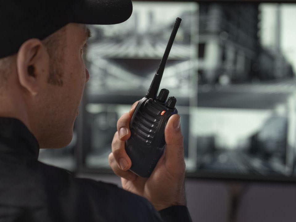 Agente de segurança operando rádio comunicador em central de portaria remota.
