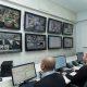 Sala de monitoramento com três pessoas acompanhando câmeras de segurança em vários monitores, representando a gestão condominial e o controle remoto de acesso.
