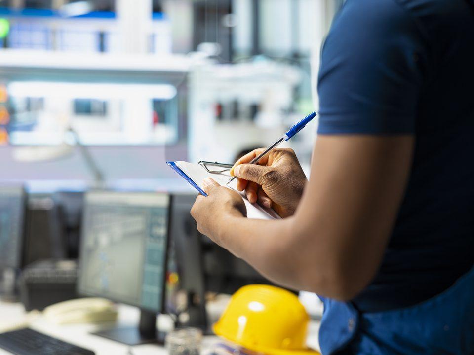 Profissional anotando informações em uma prancheta em ambiente corporativo, representando a gestão de facilities.