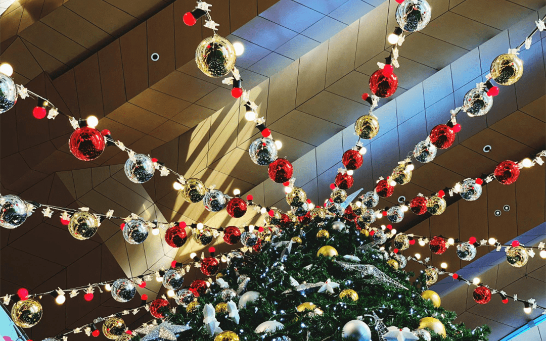 Decoração de Natal com árvore iluminada e enfeites suspensos no teto de um shopping, criando um ambiente festivo e organizado.