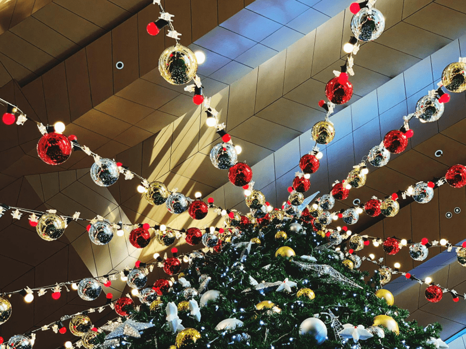 Decoração de Natal com árvore iluminada e enfeites suspensos no teto de um shopping, criando um ambiente festivo e organizado.