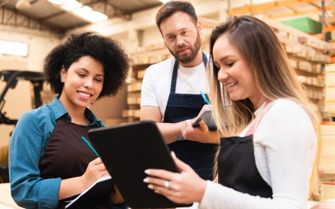 Equipe de colaboradores em área de estoque de hipermercado utilizando tablet para controle operacional e organização das atividades.