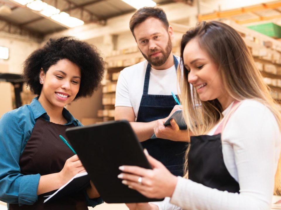 Equipe de colaboradores em área de estoque de hipermercado utilizando tablet para controle operacional e organização das atividades.