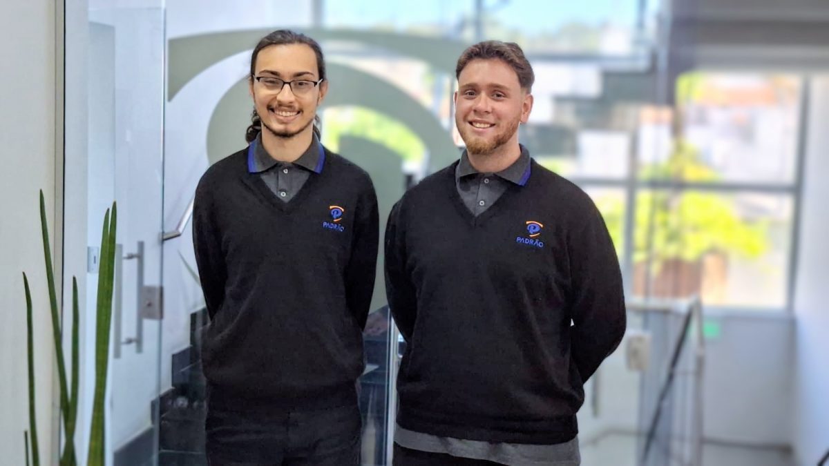 Dois jovens aprendizes da Padrão Serviços em uniforme corporativo sorrindo em ambiente interno da empresa, representando inclusão, desenvolvimento e oportunidades no mercado de trabalho.