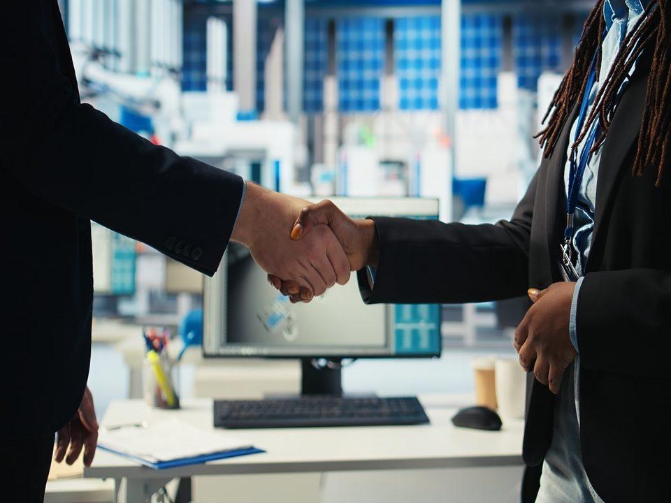 Dois profissionais apertando as mãos em ambiente corporativo industrial, simbolizando parceria estratégica e maturidade empresarial na gestão de serviços terceirizados.