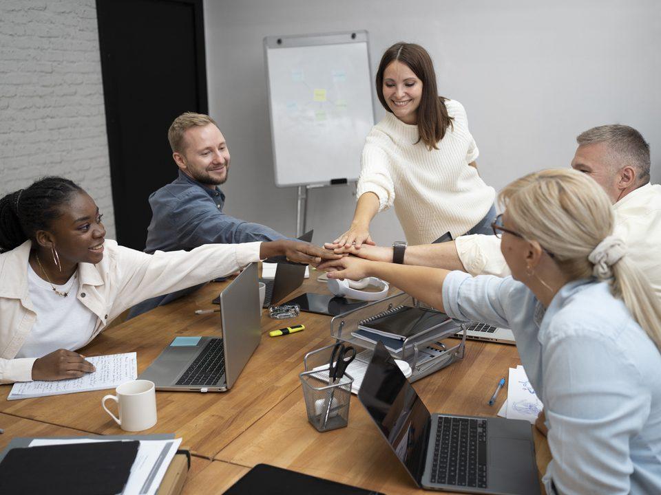 Equipe reunida em ambiente corporativo colocando as mãos juntas em sinal de colaboração, representando a importância das equipes operacionais na construção de operações eficientes e integradas.