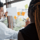 Duas pessoas analisam gráfico e escrevem em post-its colados em vidro.
