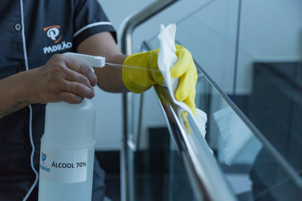 Profissional de limpeza higienizando corrimão com pano e álcool 70%
