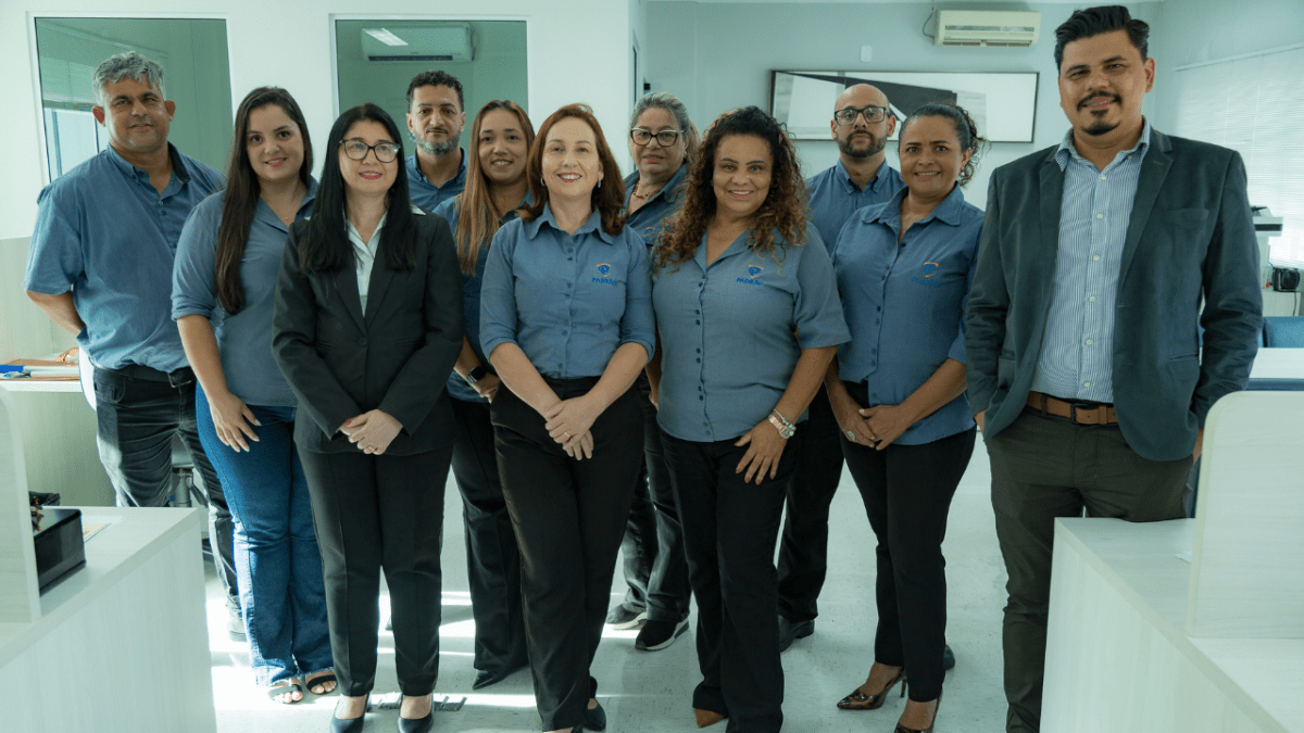 Equipe de profissionais em ambiente corporativo posa reunida, sorrindo para a câmera.