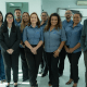 Equipe de profissionais em ambiente corporativo posa reunida, sorrindo para a câmera.