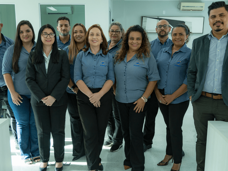 Equipe de profissionais em ambiente corporativo posa reunida, sorrindo para a câmera.