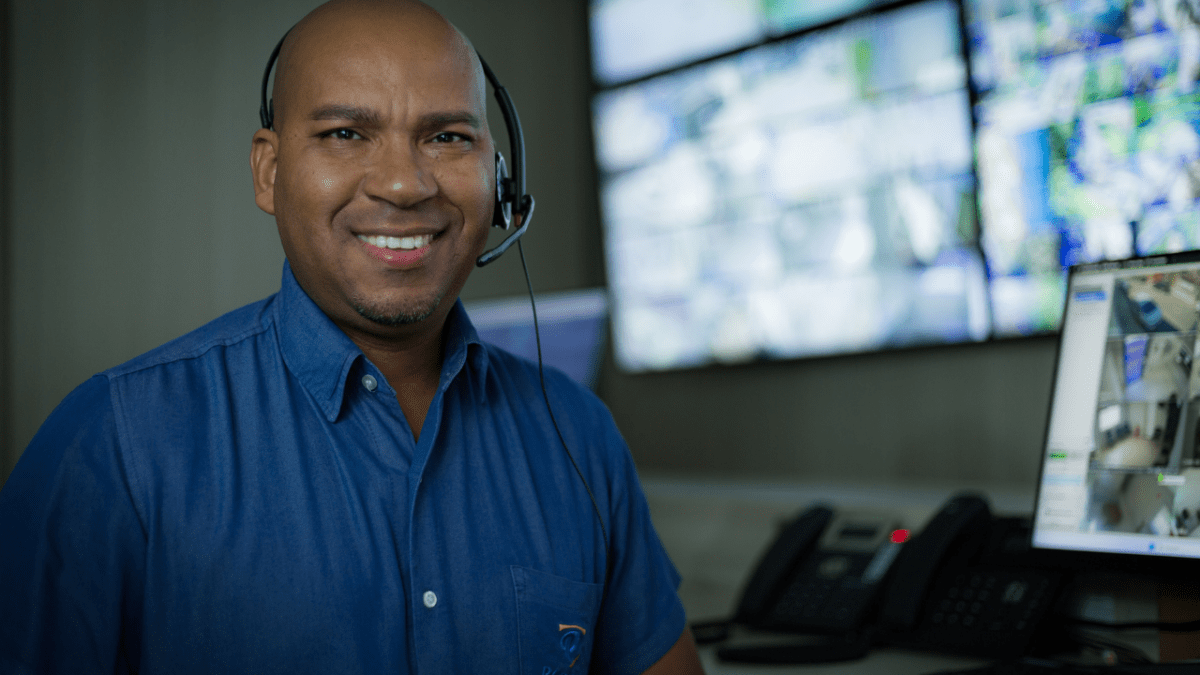 Profissional de monitoramento usando headset em central de segurança com telas de vigilância ao fundo.