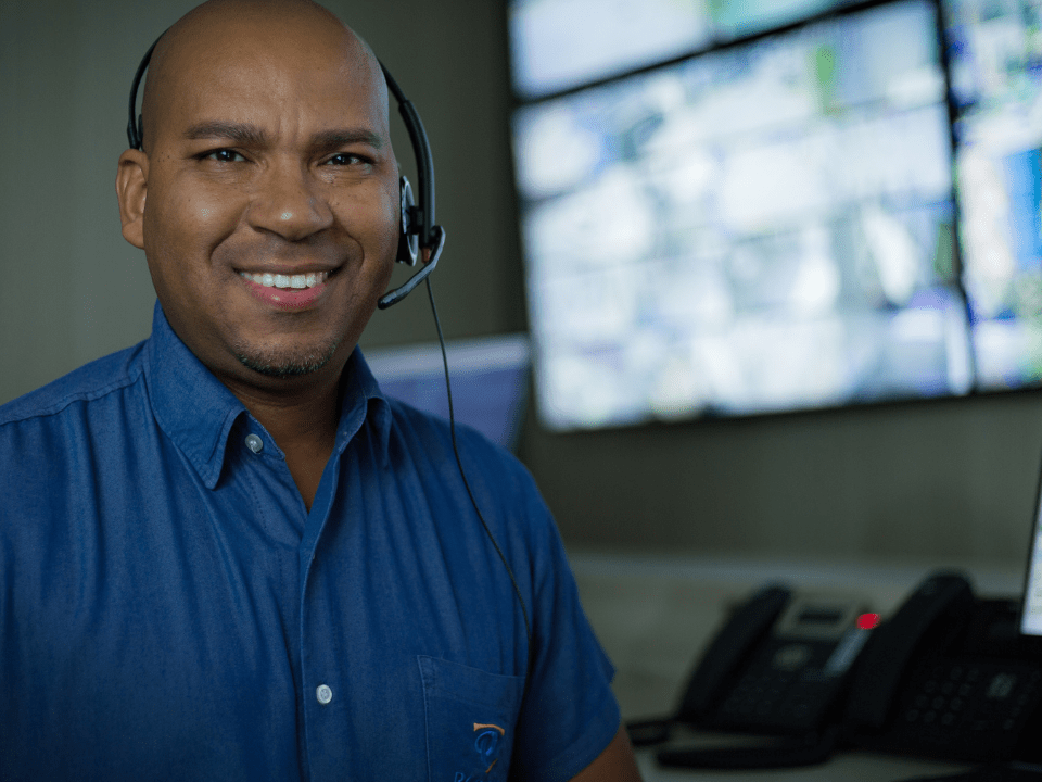 Profissional de monitoramento usando headset em central de segurança com telas de vigilância ao fundo.