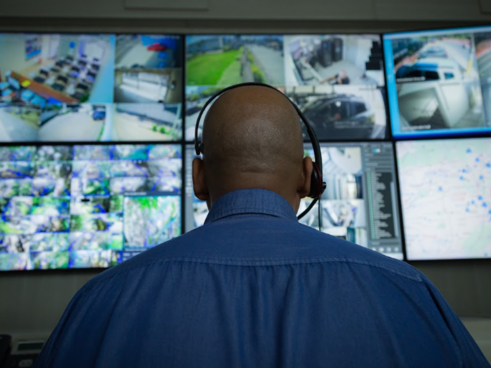 Operador monitora câmeras de segurança em uma central de vigilância com múltiplos monitores.