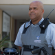 Vigilante uniformizado em frente a um edifício, utilizando rádio comunicador e colete de segurança.