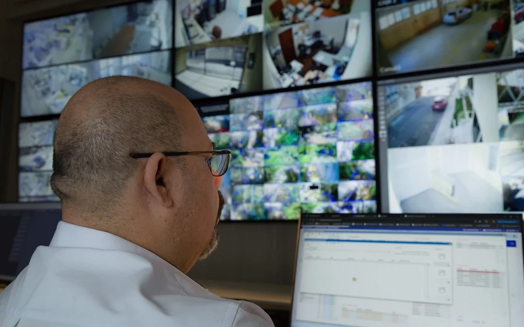 Profissional monitora câmeras de segurança em uma central de controle, atividade relacionada à gestão de facilities.