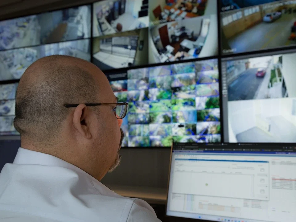 Profissional monitora câmeras de segurança em uma central de controle, atividade relacionada à gestão de facilities.